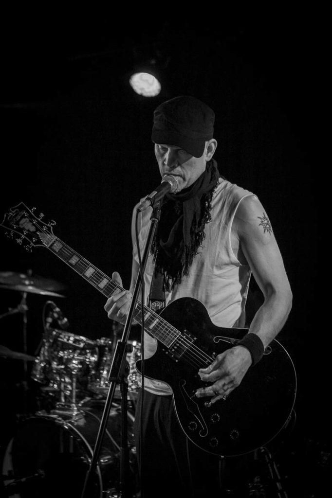 Kuvassa artisti SPK Toivonen lavalla, soittamassa kitaraa mustavalkoisena
