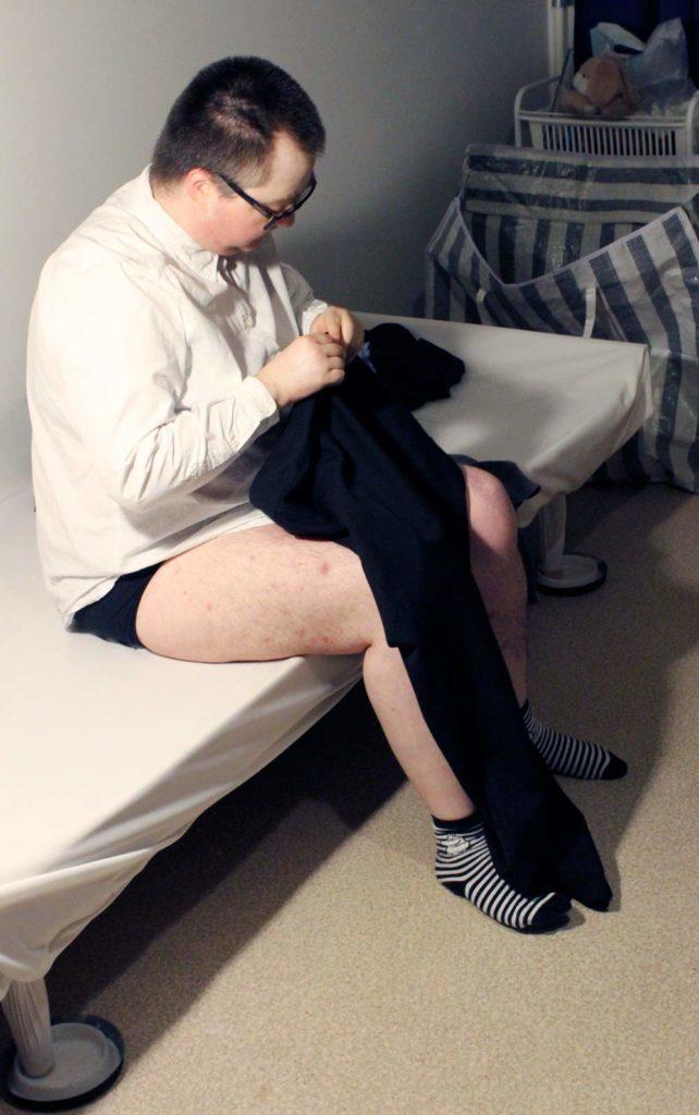 mies istuu sängyn reunalla ja kääntää housuja