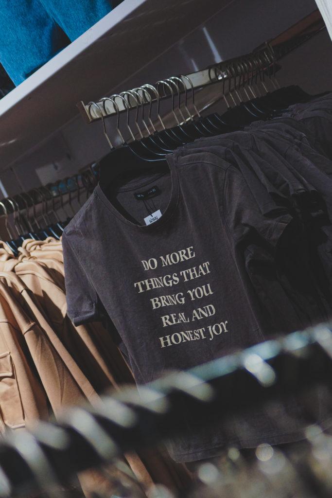 Kuva vaatekaupasta. Kuvassa T-paitoja, joissa teksti "Do more things that bring you real and honest joy".