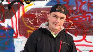 Mies seisoo graffitimaalatun seinän edessä ja hymyilee kameralle.